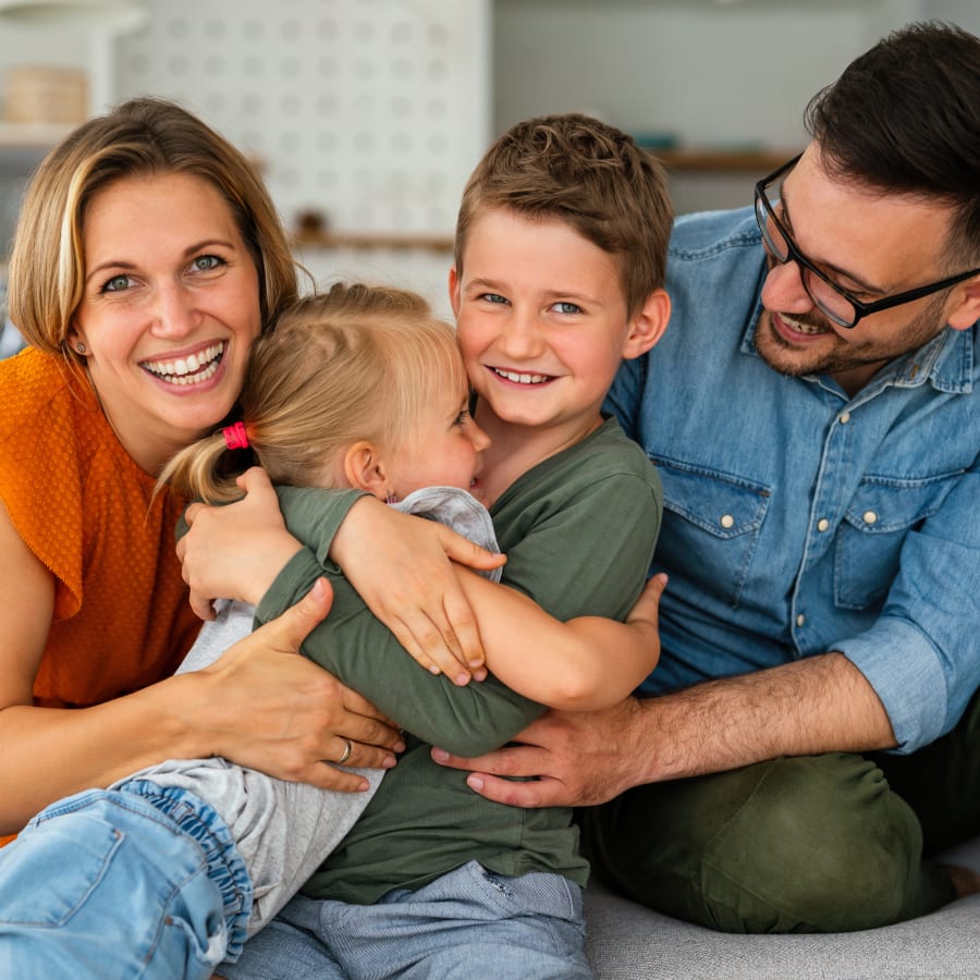 A young family of four is laughing and embracing one another.