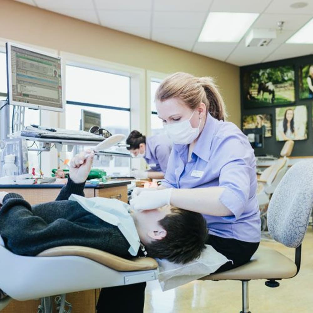 A team member performs an examination on a young boy's mouth as he lays back in a treatment chair.