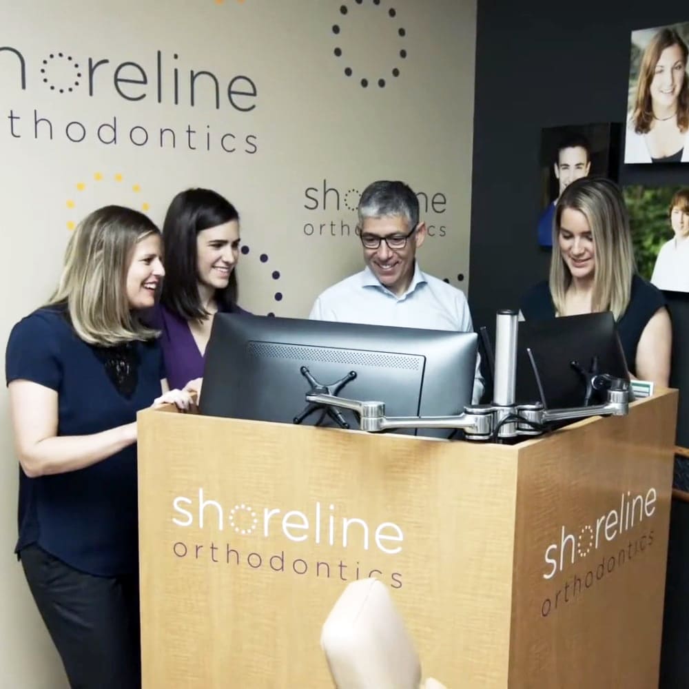 The Shoreline Orthodontics team standing around a desk looking at the computer.